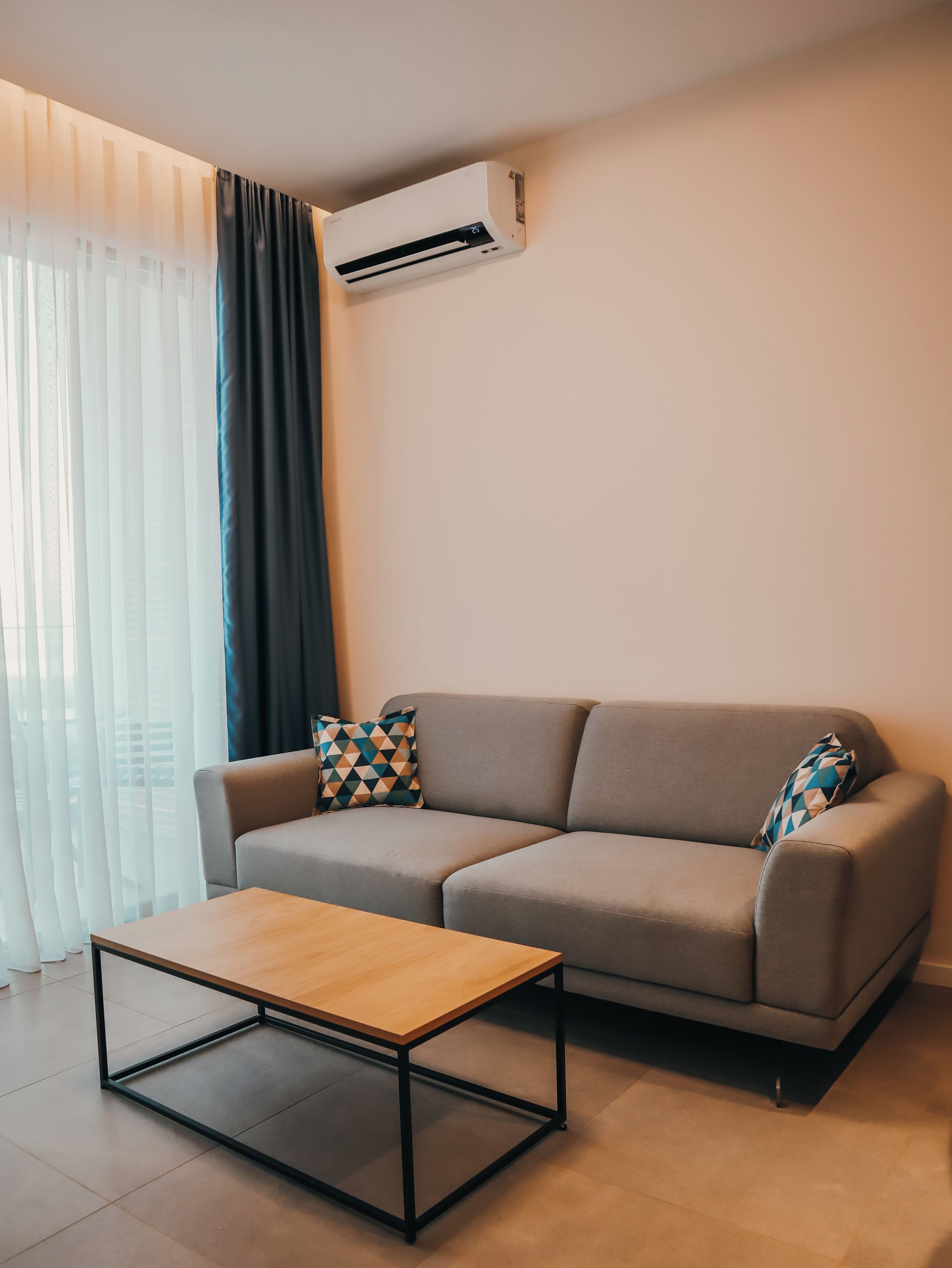 A modern living room with a sofa, a coffee table, and an air conditioning unit.