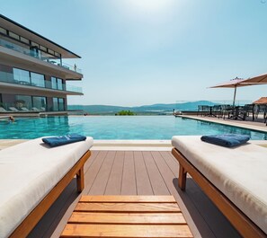 Un área de piscina con dos sillas reclinables, una terraza de madera y vistas a montañas.