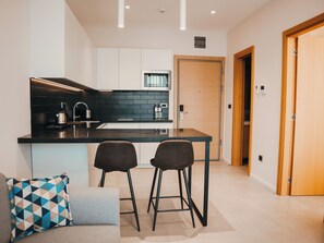 A modern kitchen with a central island, two bar stools, a coffee machine, and a built-in oven. - Royal Blue Resort And Residences (Kotor)