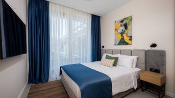 A hotel room with a bed, a nightstand, a painting, and a window with curtains.