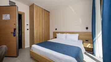A hotel room with a bed, a wardrobe, a desk, and a window with curtains.