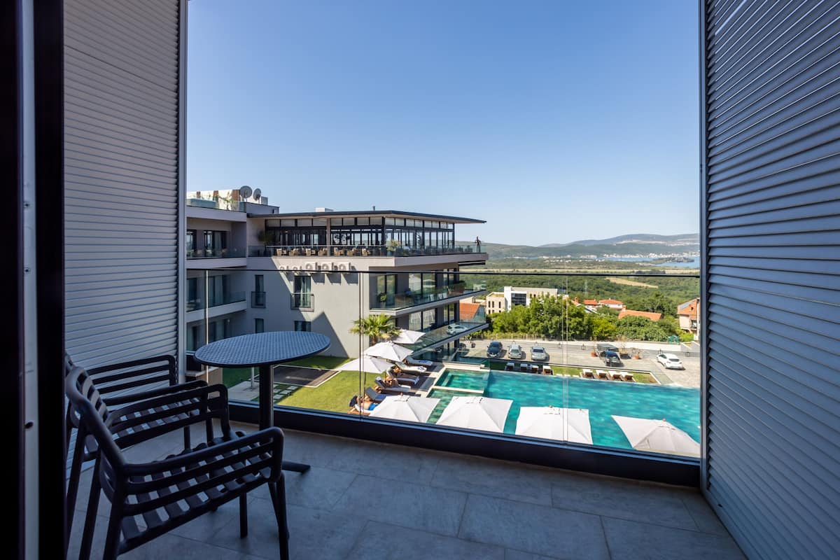 Un balcón con piscina, mobiliario exterior y vistas a un edificio moderno y un paisaje.
