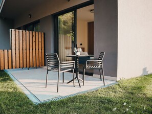 An outdoor patio with two chairs and a table, a wooden fence, and a glass door leading to an interior space. - Royal Blue Resort And Residences (Kotor)