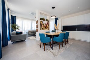 Una sala moderna con un sofá, una mesa de comedor con sillas, una zona de cocina con armarios y un amplio ventanal con cortinas.