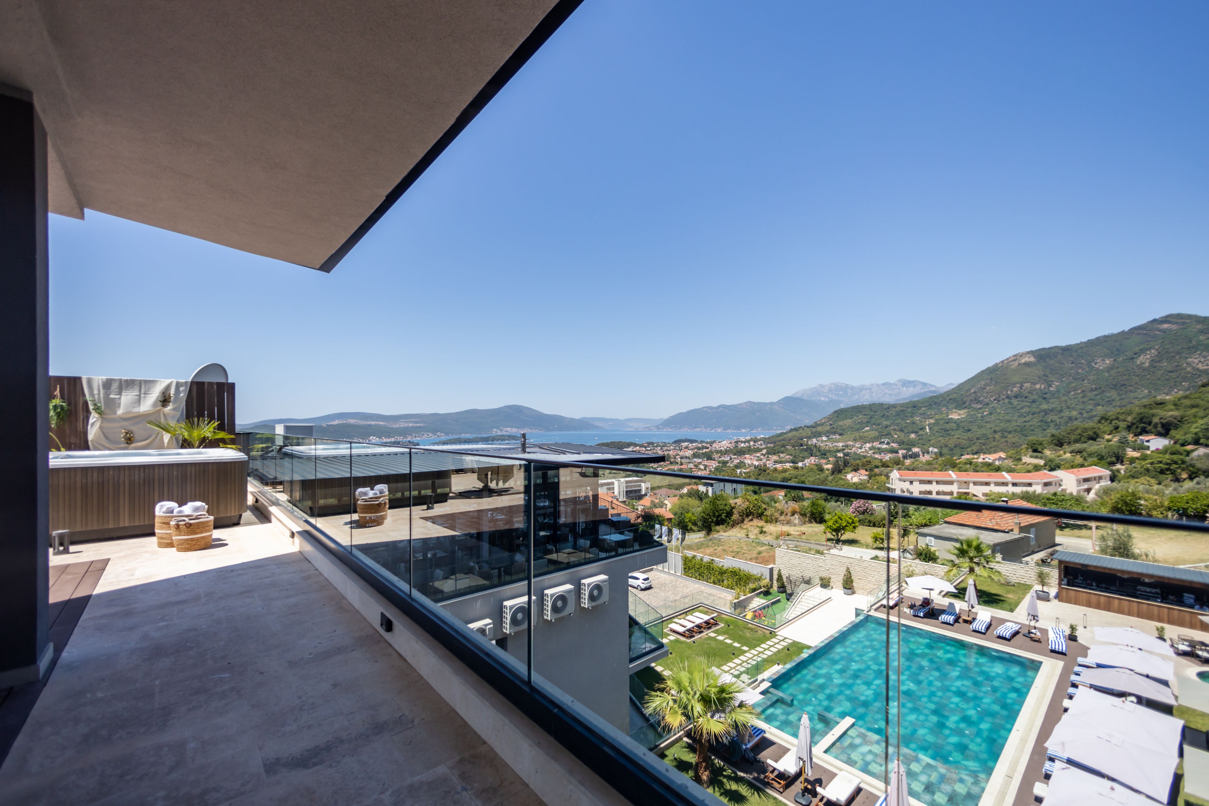 Ein Balkon mit Glasgeländer mit Blick auf einen Pool und eine Berglandschaft.