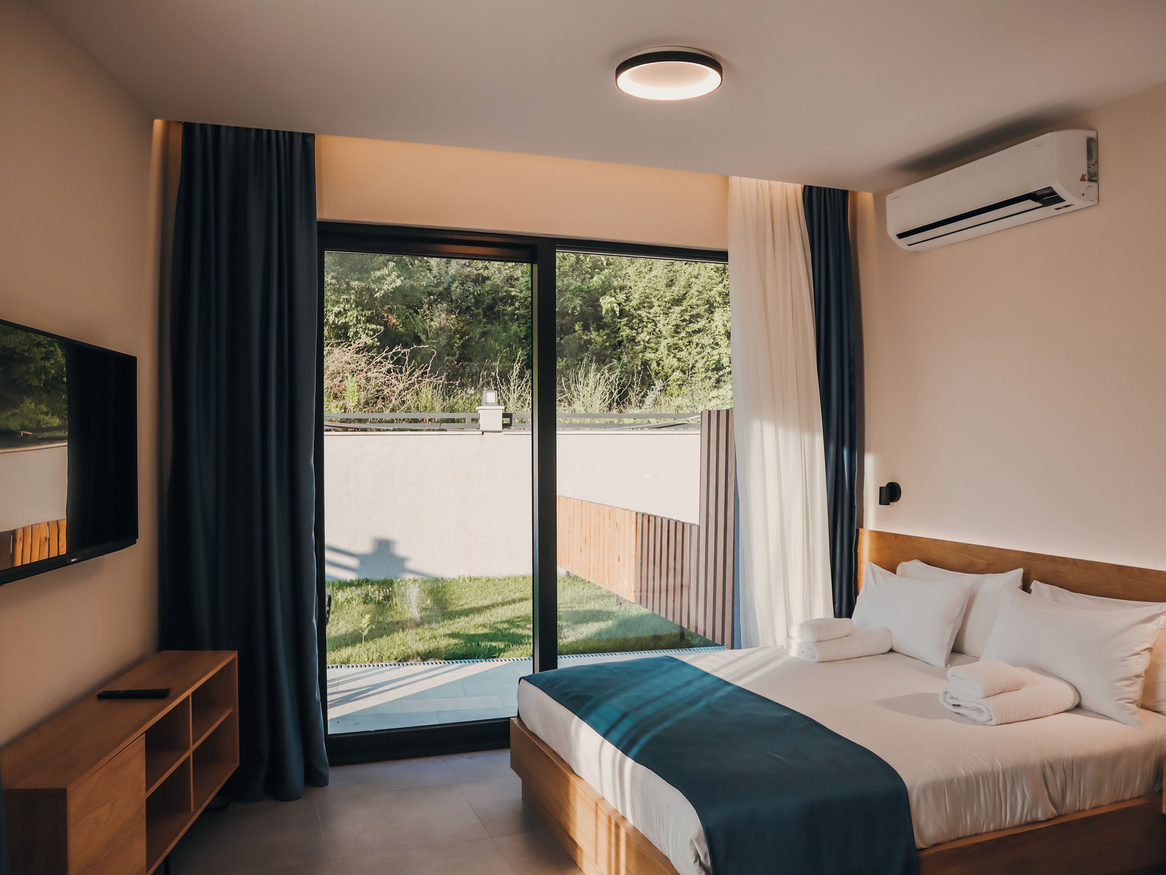 A bedroom with a bed, a TV, a window with curtains, and an air conditioner.