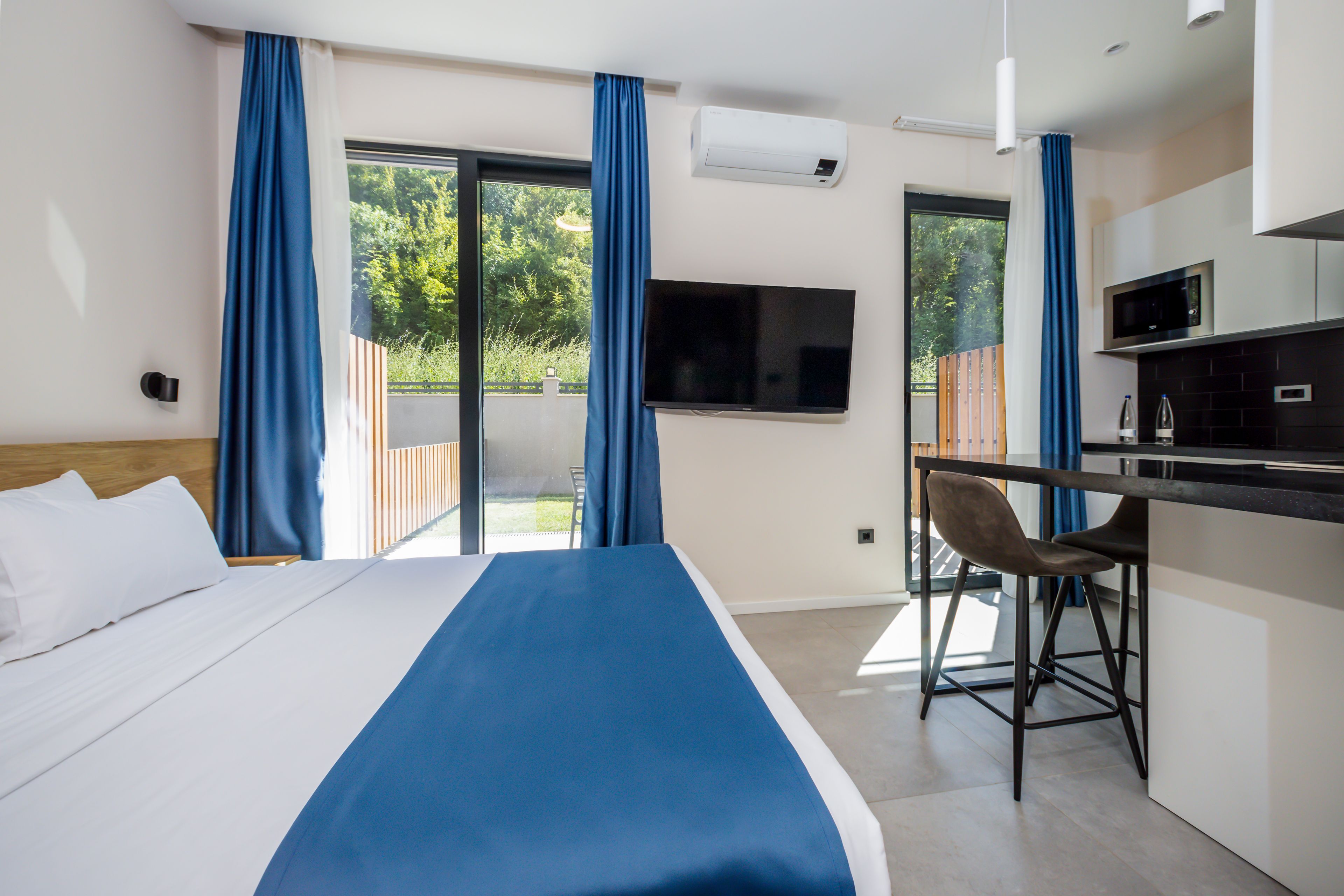 A hotel room with a bed, a desk, a TV, and a view of the outdoors.