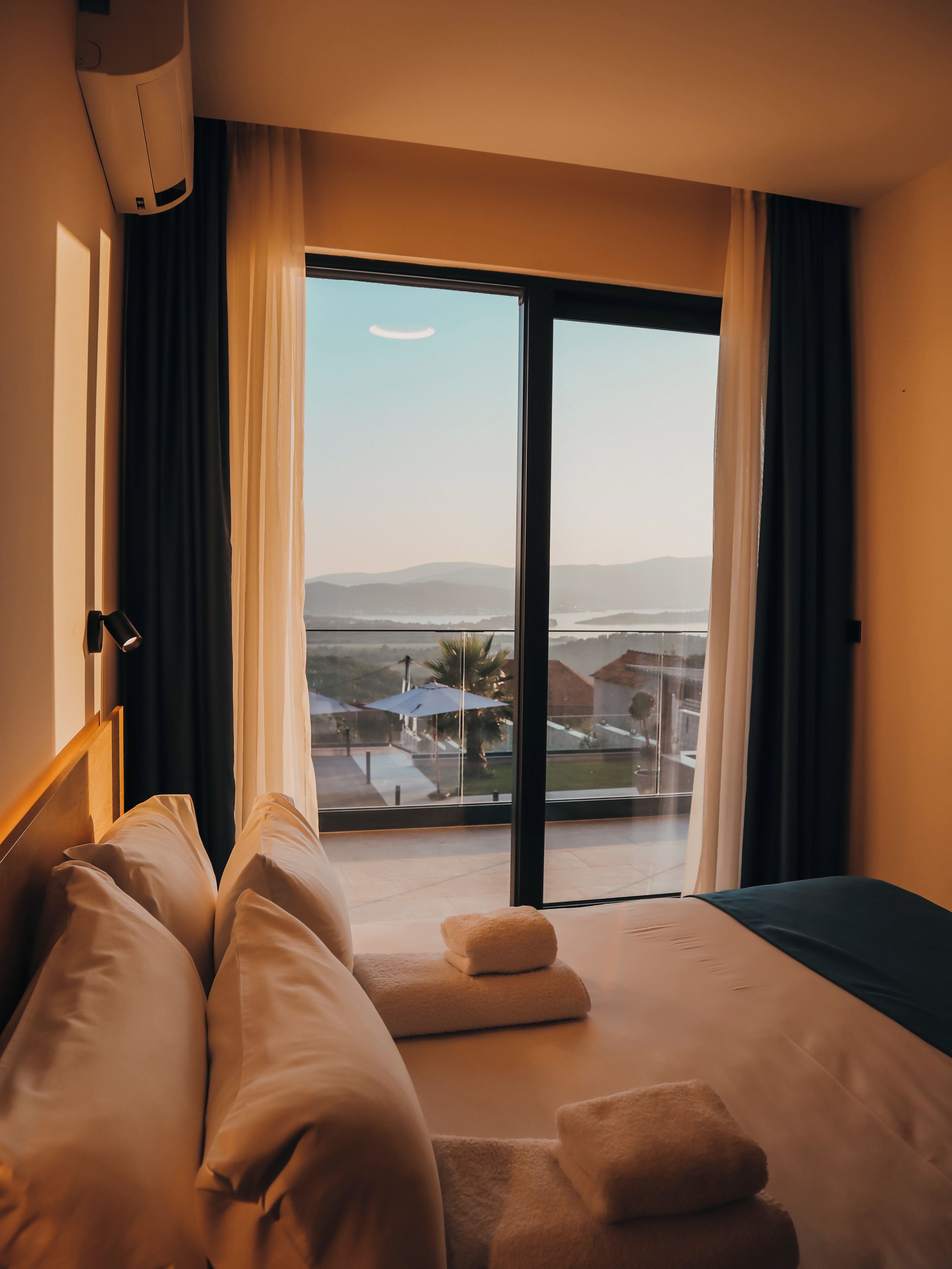 Una habitación de hotel con cama, ventana con cortinas, vistas al paisaje y un equipo de aire acondicionado.