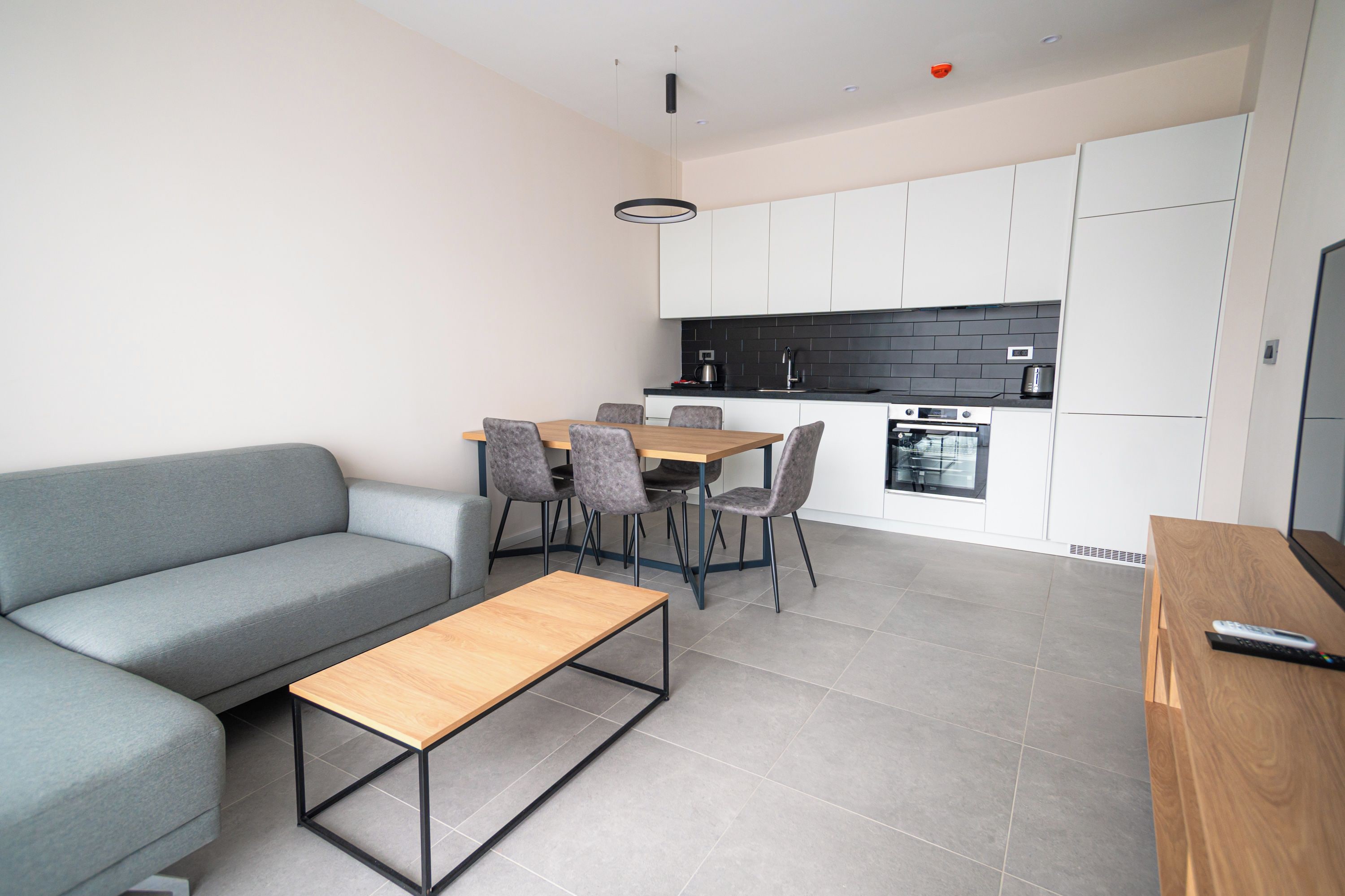 A modern living room with a sofa, a coffee table, and a dining area with chairs and a table.