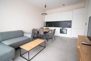 A modern living room with a sofa, a coffee table, and a dining area with chairs and a table. - Royal Blue Resort And Residences (Kotor)