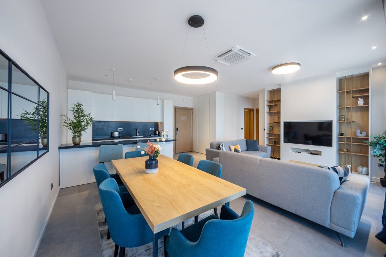 A modern living room with a sofa, a TV, and a dining area with a table and chairs.