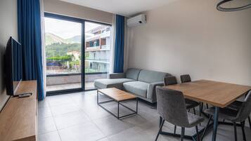 Uma sala de estar moderna com um sofá, uma mesa de jantar e cadeiras. Há uma TV em um suporte, e um aparelho de ar condicionado na parede.
