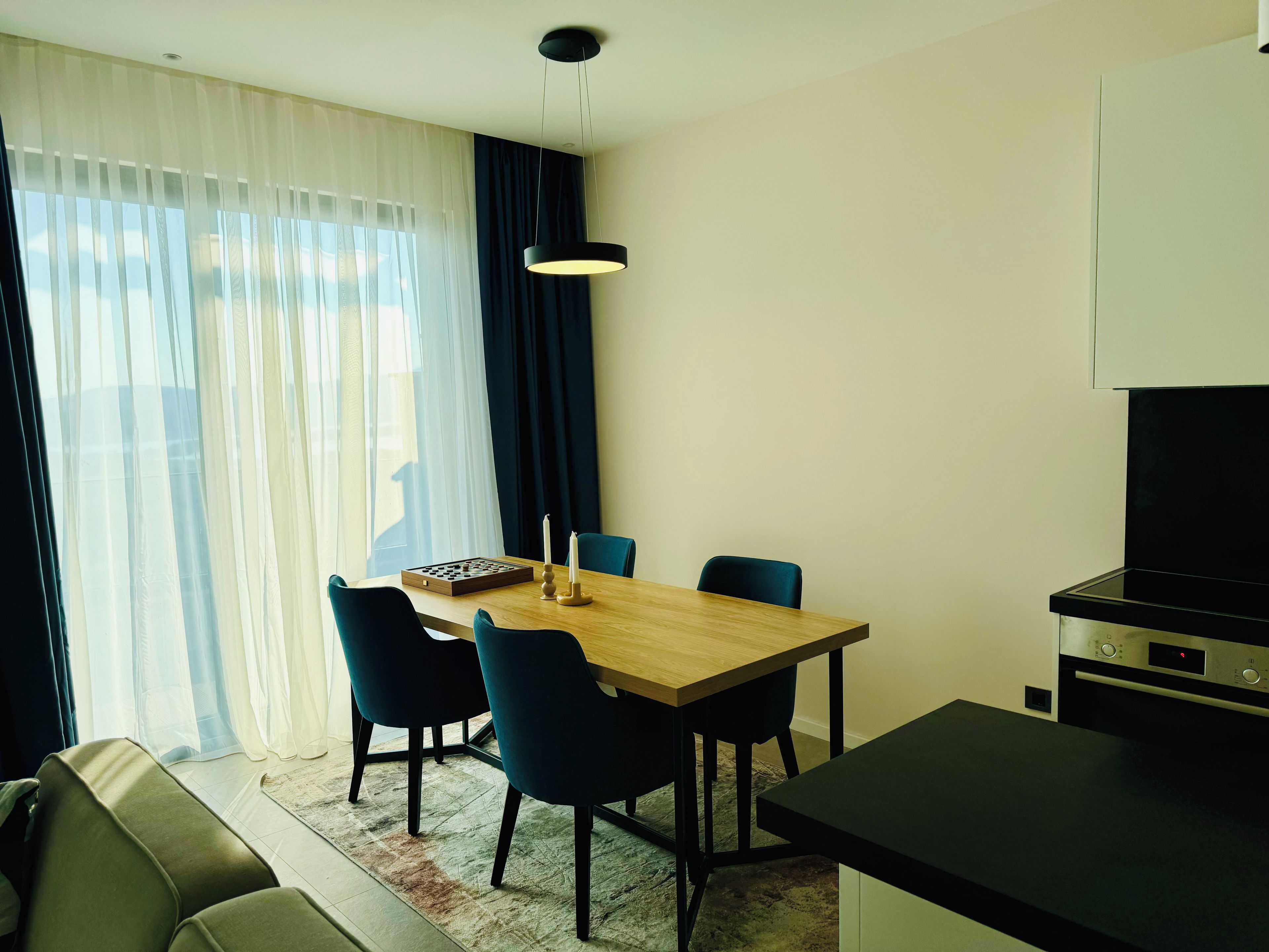 Un espace repas moderne avec une table en bois, quatre chaises, un jeu d’échecs et une bougie.