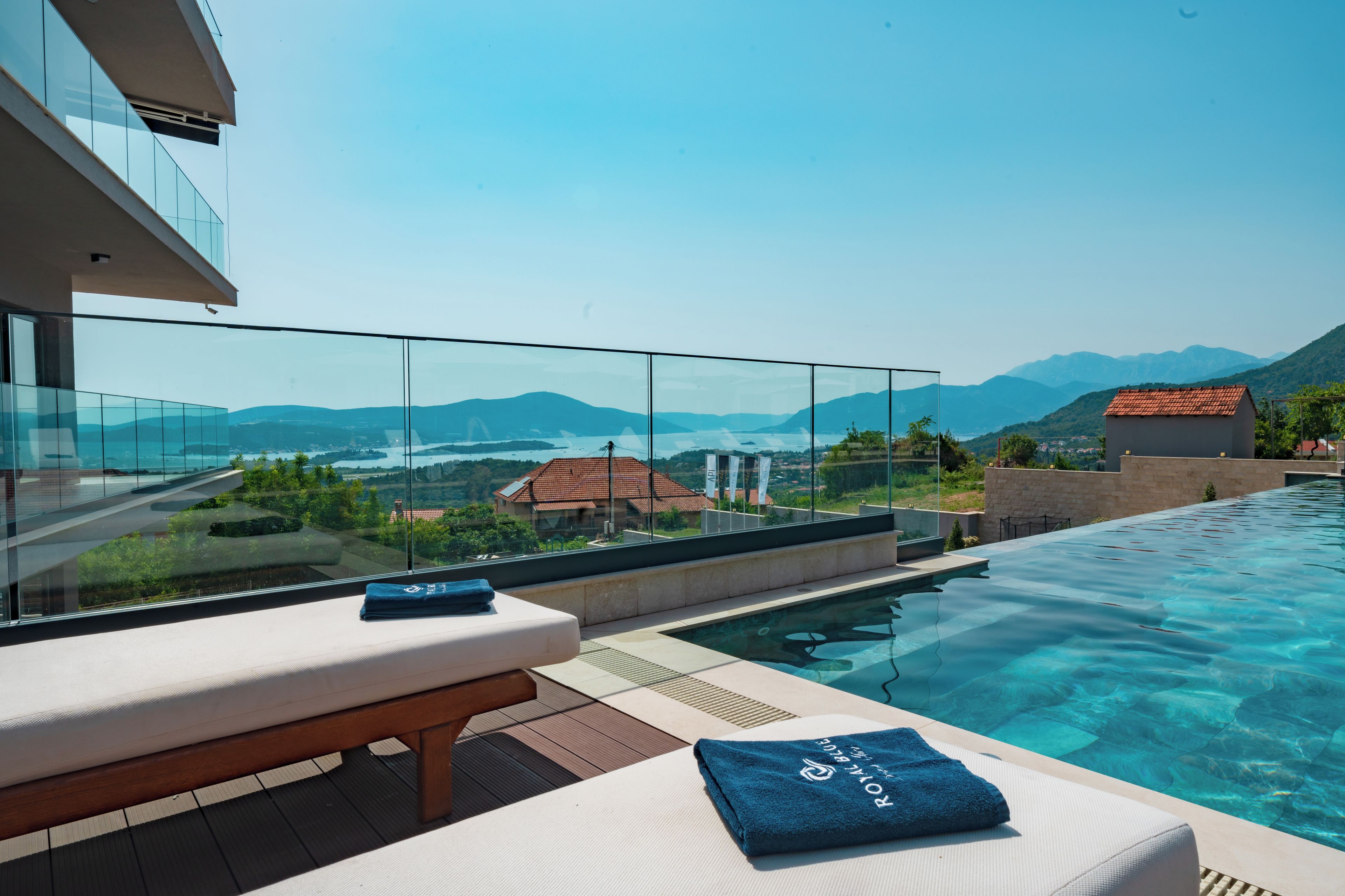 A modern infinity pool with clear water, a wooden deck, and a lounge area with a bench and towels.