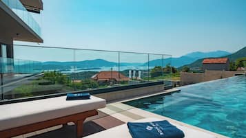 A modern infinity pool with clear water, a wooden deck, and a lounge area with a bench and towels.