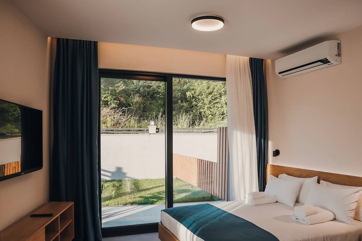Un dormitorio con cama, televisión, ventana con cortinas y aire acondicionado.