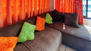 A sectional sofa with colorful pillows, a window with curtains, and a tiled floor.