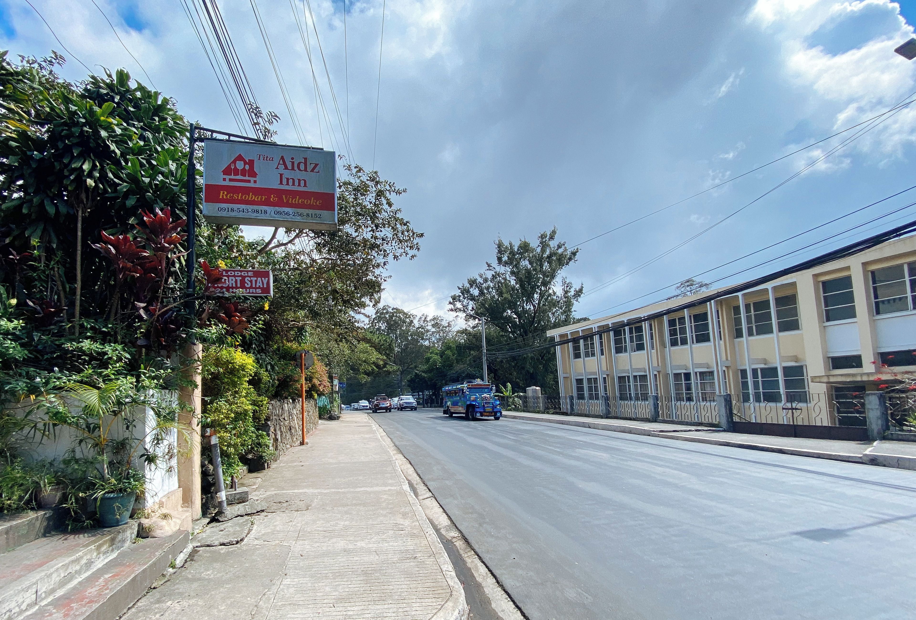 A street view with a Tita Aidz Inn sign, a sidewalk, and a building with multiple windows.