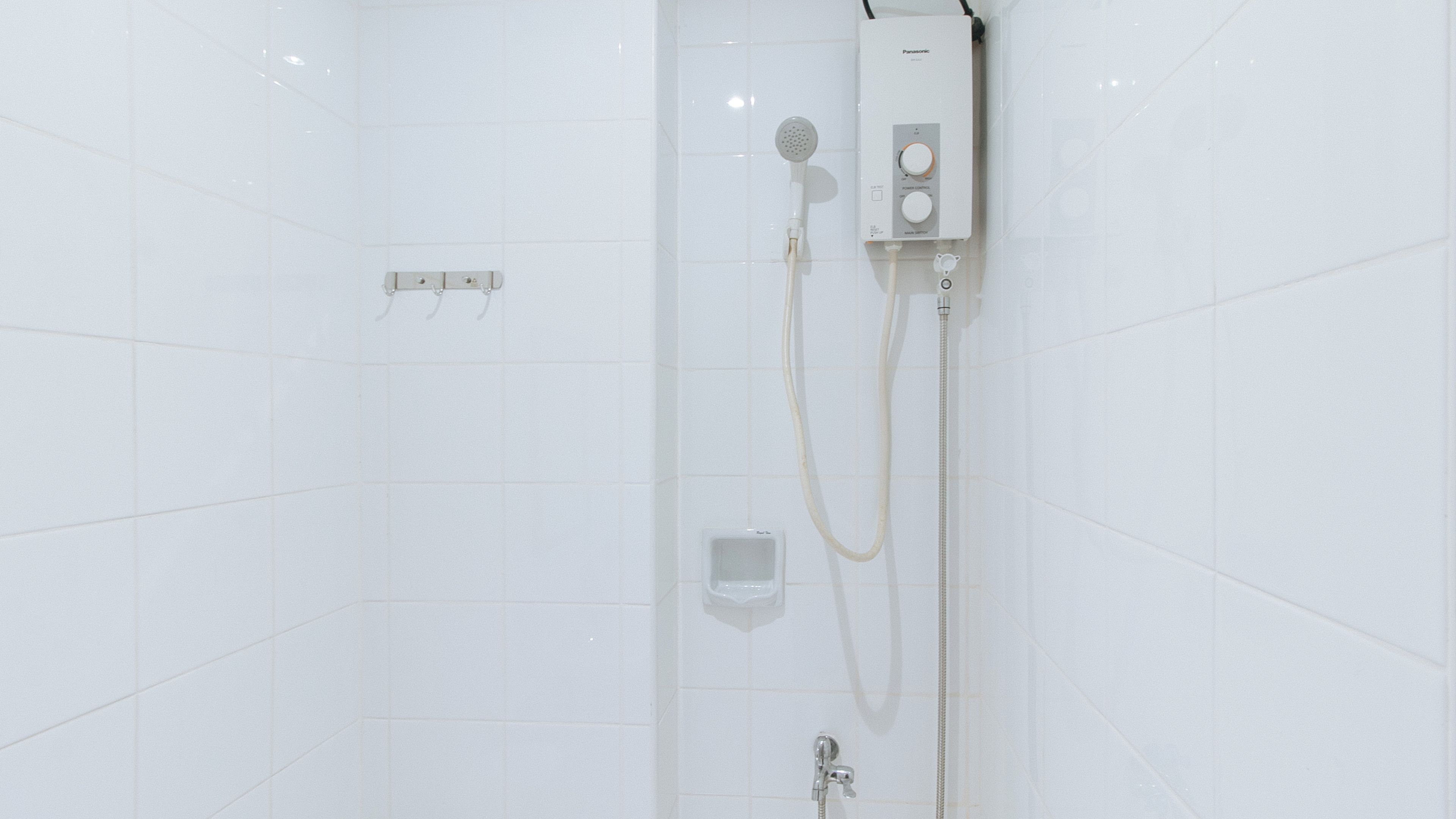 A white tiled shower enclosure with a handheld showerhead, a wall-mounted control panel, and a handheld shower hose.