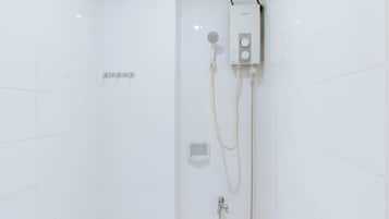 A white tiled shower enclosure with a handheld showerhead, a wall-mounted control panel, and a handheld shower hose.