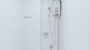 Une cabine de douche carrelée de carreaux blancs, dotée d’un pommeau de douche à main, d’un panneau de commande fixé au mur et d’un flexible de douche à main.