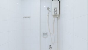A white tiled shower enclosure with a handheld showerhead, a wall-mounted control panel, and a handheld shower hose.
