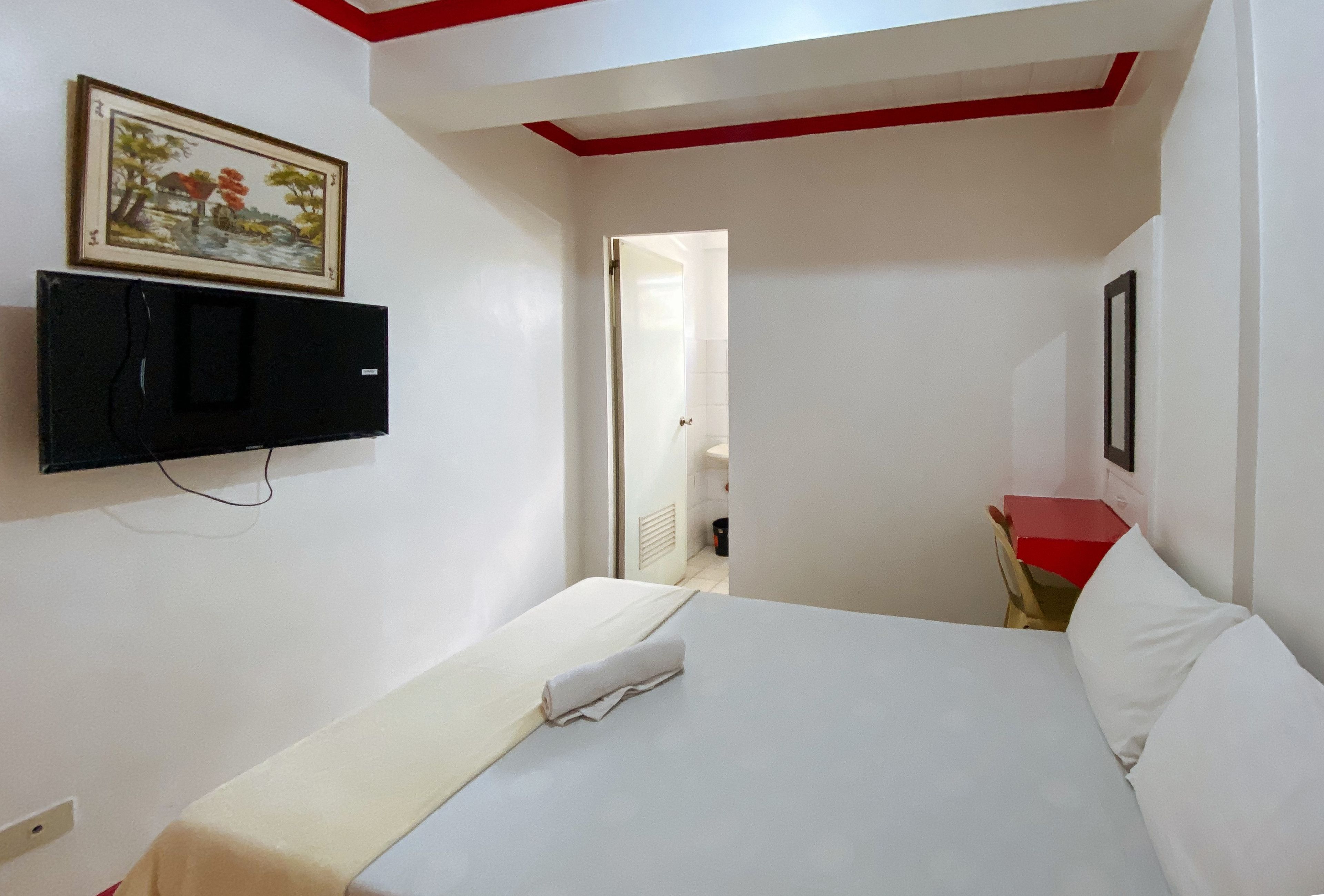 Ein Hotelzimmer mit einem Bett, einem an der Wand montierten Fernseher und einem Gemälde über dem Bett.