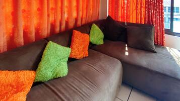 Ein modulares Sofa mit bunten Kissen, ein Fenster mit Vorhängen und ein gefliester Boden.