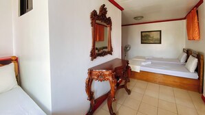 A hotel room with a bed, a wooden nightstand, a mirror, a bedside table, a fan, and a painting on the wall.