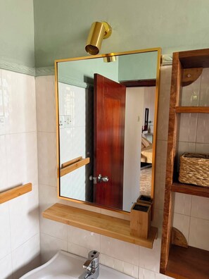 A bathroom with a large mirror, a wooden shelf, a towel rack, and a bathtub. - Riverbank Bentota (Aluthgama)