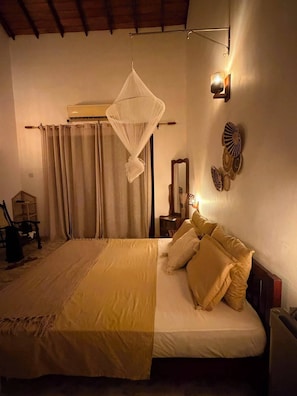 A bedroom with a bed, curtains, a bedside table, a mirror, and wall-mounted decorative items. - Riverbank Bentota (Aluthgama)