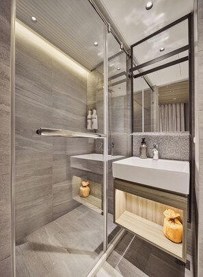 Un baño moderno con cabina de ducha de vidrio, tocador con espejo y estante de madera.