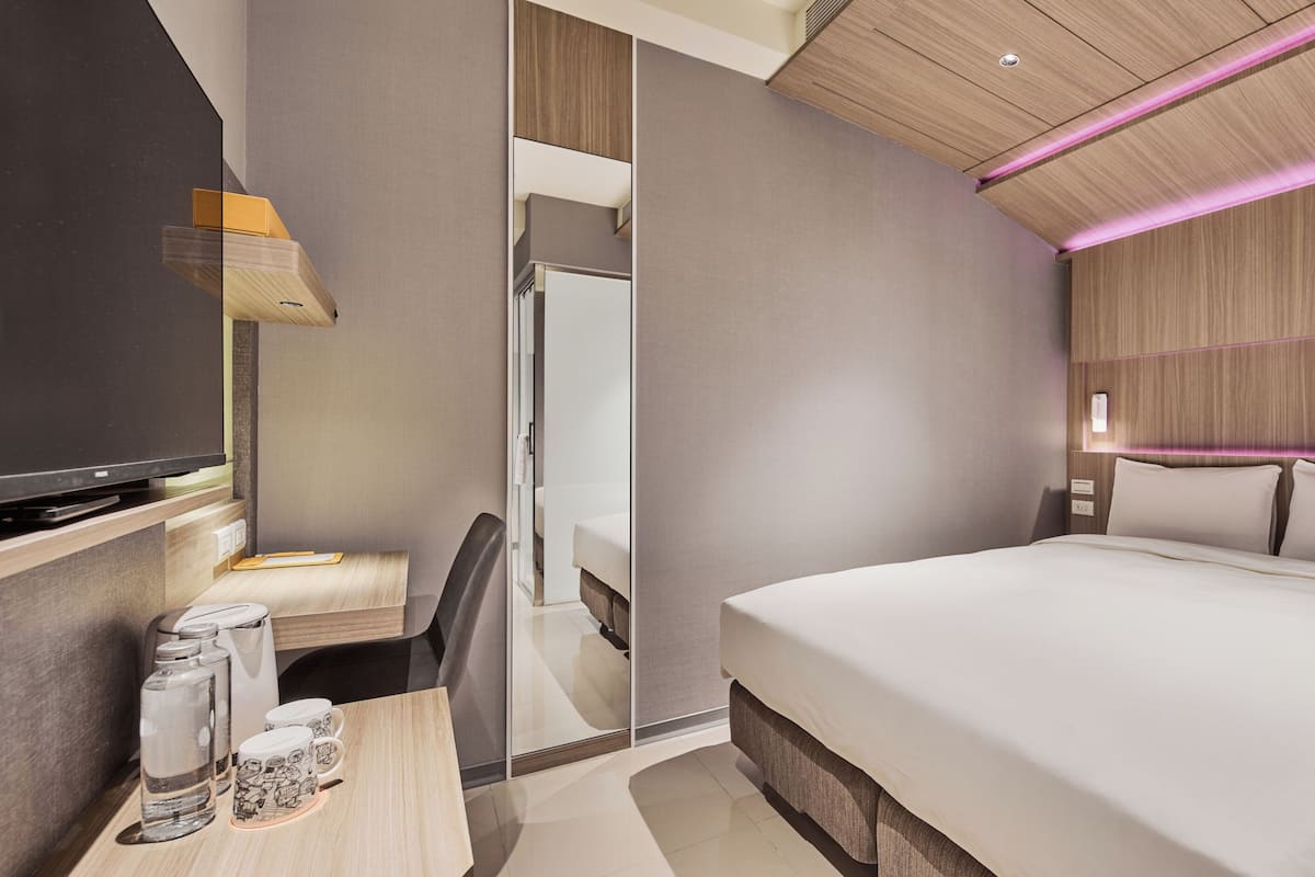 Una habitación de hotel moderna con una cama grande, un escritorio con una silla, un televisor y un espejo.