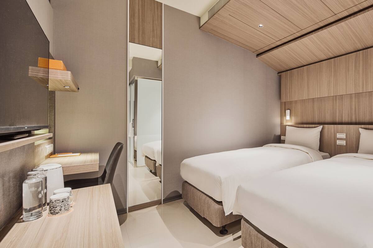 Una habitación de hotel moderna con techo de madera, dos camas, un escritorio con silla y un espejo.