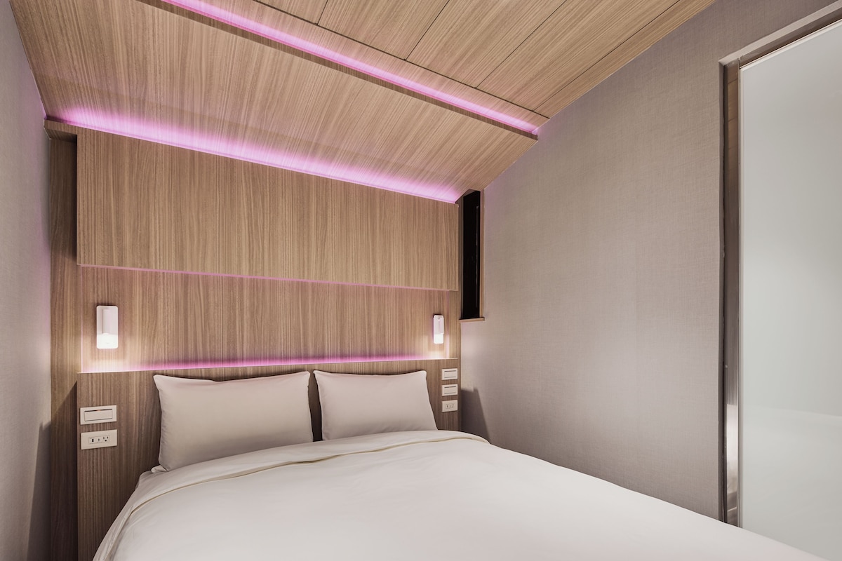 Una habitación de hotel moderna con cabecera de madera, lámparas de noche y una paleta de colores neutros.