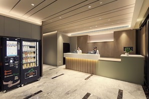 A reception area with a reception desk, two receptionists, and a vending machine. - Orange Hotel - Hanzhong Taipei (Taipei)