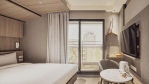 A hotel room with a bed, a seating area with a table, a TV, and a view of buildings through the window. - Orange Hotel - Hanzhong Taipei (Taipei)