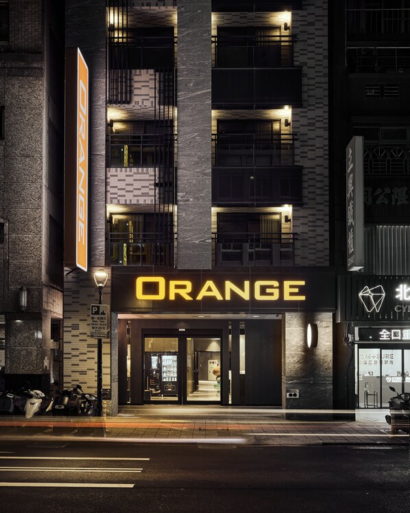 Un edificio con un llamativo letrero 'ORANGE', un cartel de estacionamiento y un escaparate con entrada de vidrio.