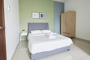 A neatly made bed with white linens and a grey headboard, a wooden wardrobe, and two framed pictures on the wall.