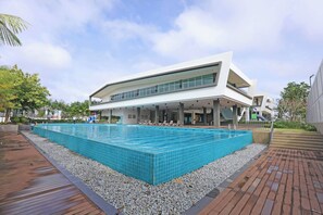 Un edificio moderno con piscina, mobiliario exterior y una zona cubierta.
