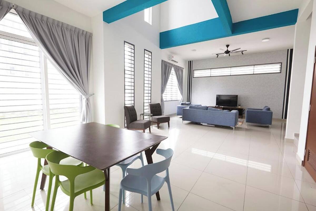 A modern living room with a dining area, a sofa set, a flat-screen TV, and large windows with curtains.