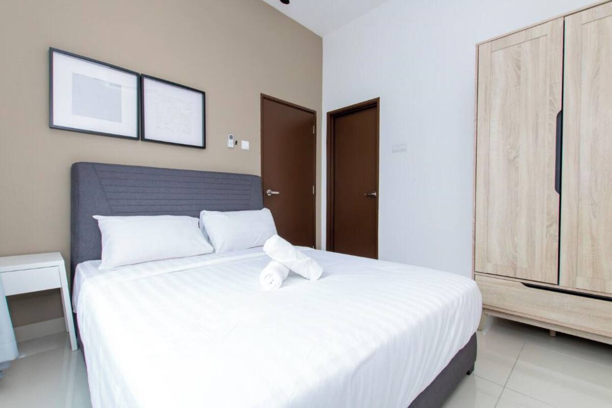 A neatly made bed with white linens, a grey headboard, and a wooden wardrobe with a light finish.