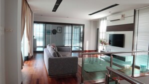 Een moderne woonkamer met een bank, een televisie en een balkon met een hekwerk.
