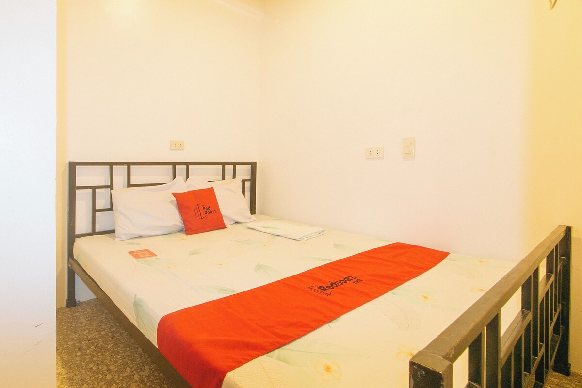 A single bed with a metal frame, white bedding, and a red blanket.