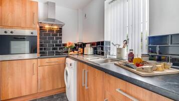 A modern kitchen with wooden cabinets, a built-in oven, a dishwasher, and a large window with blinds.