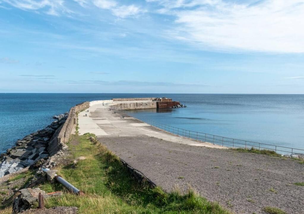A coastal promenade with a concrete walkway, a rocky shoreline, and a calm sea.