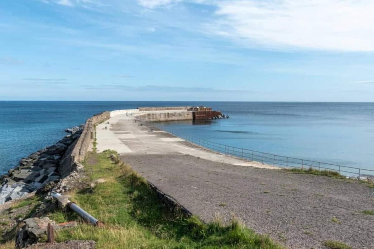 A coastal promenade with a concrete walkway, a rocky shoreline, and a calm sea.