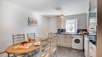 A compact kitchen with a dining table, chairs, a washing machine, and a window.