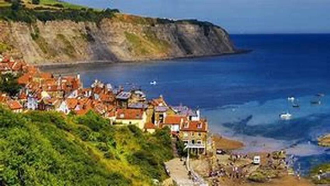 A coastal town with buildings along the cliffside, a beach, and boats in the water.