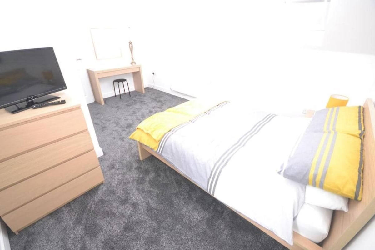 Quarto com cama, escrivaninha, televisão e uma cadeira.